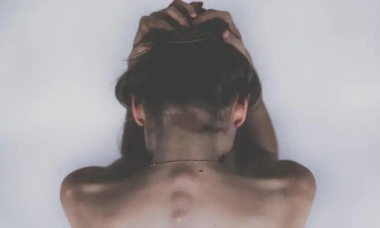 Mulher com a mão nas costas na altura da escápula, dor por nervo escapular inflamado